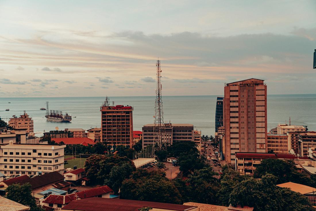 Freetown skyline with office towers, a telecom mast and ships in the harbour at dusk
