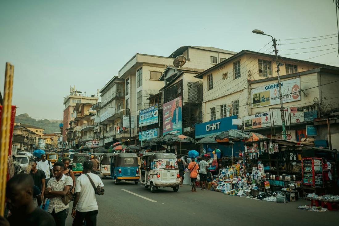 Busy commercial street with tuk-tuks, market stalls and money transfer signs
